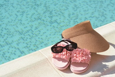 Stylish visor cap, slippers and sunglasses near outdoor swimming pool on sunny day, space for text