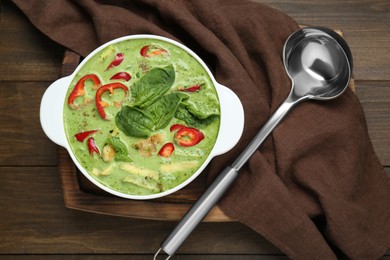 Photo of Saucepan with delicious green curry chicken soup and ladle on wooden table, flat lay