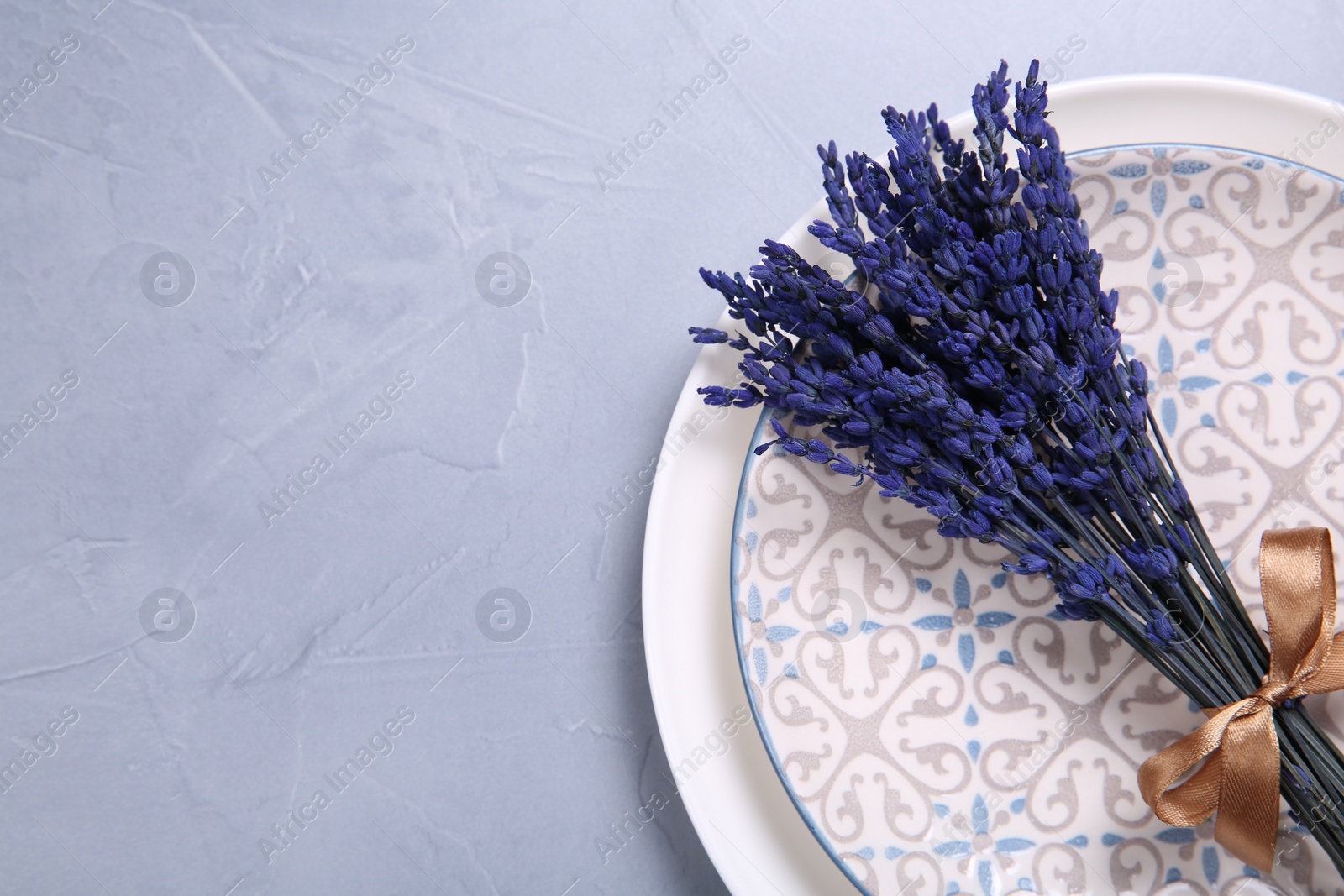 Photo of Bouquet of beautiful preserved lavender flowers and plates on light grey textured table, top view. Space for text