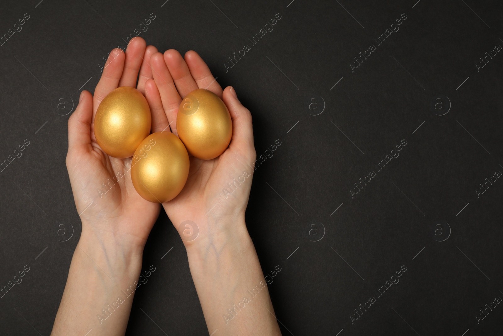 Photo of Woman holding shiny golden eggs on black background, top view. Space for text