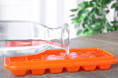 Photo of Pouring water into ice cube tray on wooden table, closeup