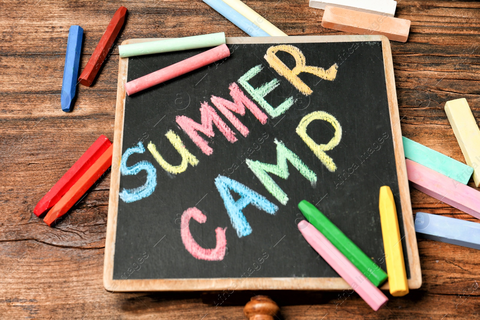 Photo of Little blackboard with text SUMMER CAMP chalked in different colors on table