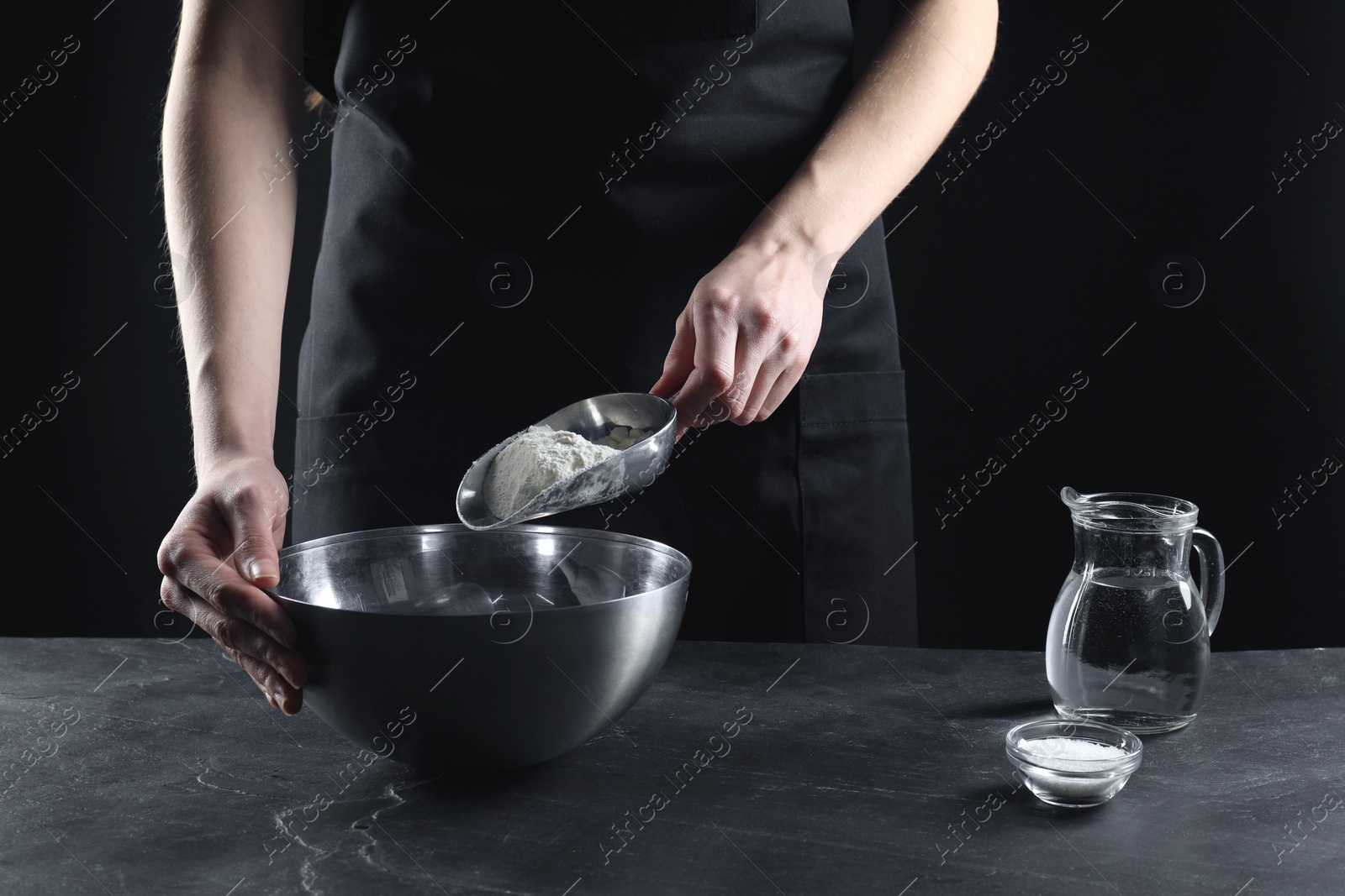 Photo of Making bread. Woman putting flour into bowl at grey textured table, closeup