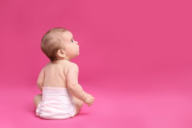 Photo of Cute little baby in diaper sitting on pink background, back view. Space for text
