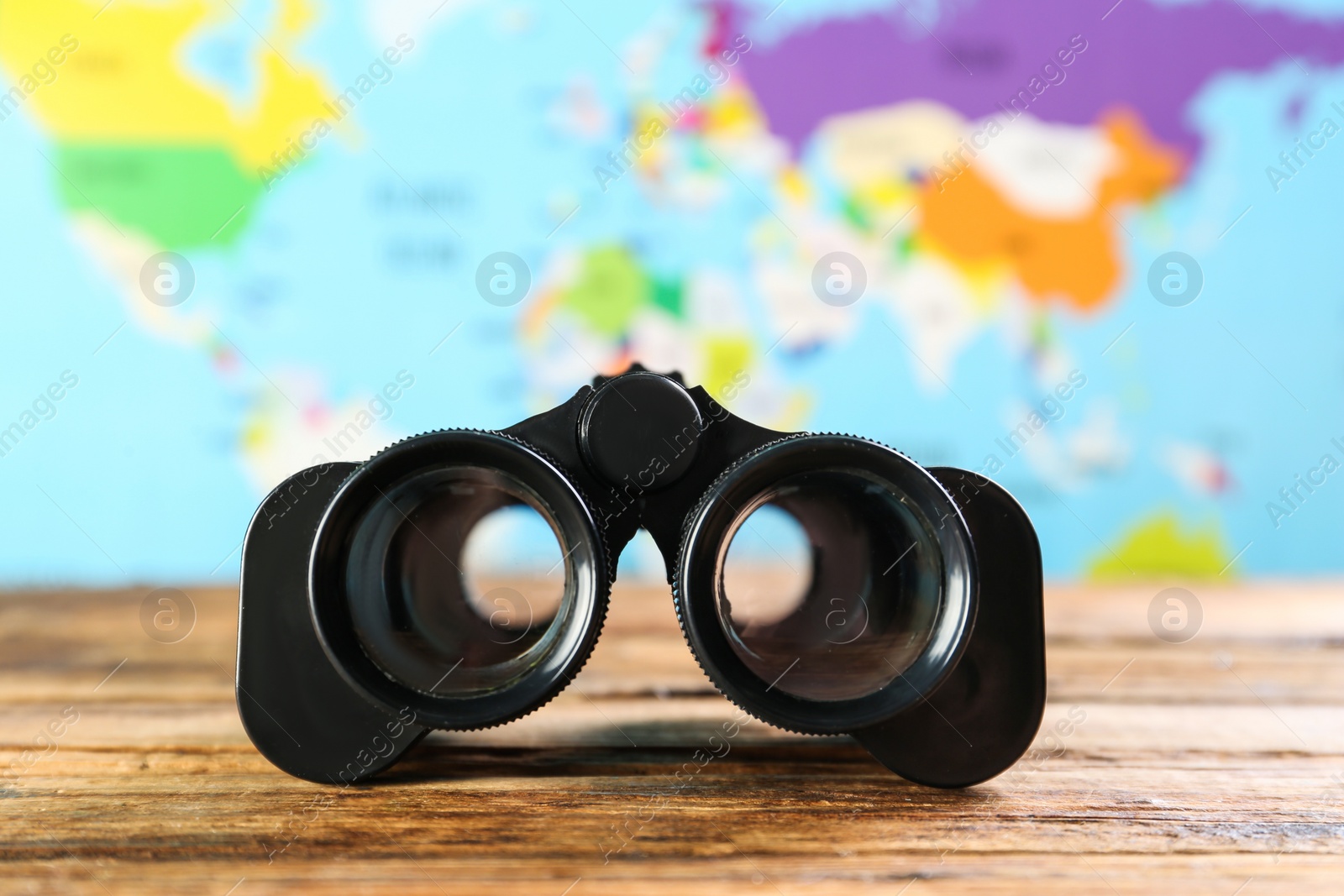 Photo of Modern binoculars on wooden table against blurred map