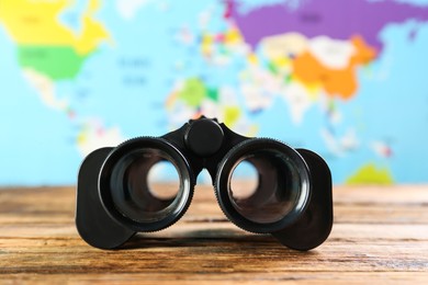 Photo of Modern binoculars on wooden table against blurred map