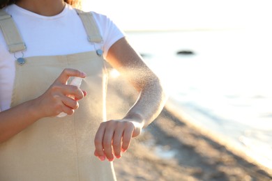 Photo of Young woman using insect repellent on beach, closeup