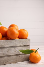 Delicious tangerines with leaves on light wooden table