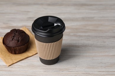 Photo of Paper cup with black lid and muffin on wooden table, space for text. Coffee to go