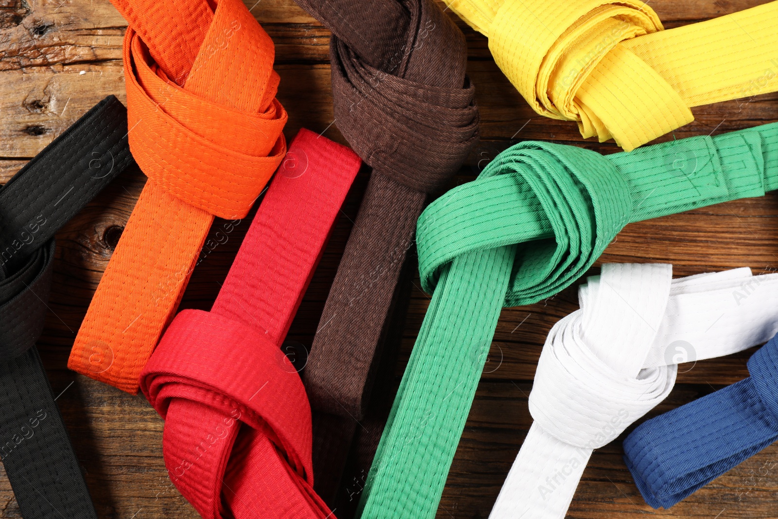 Photo of Colorful karate belts on wooden background, flat lay