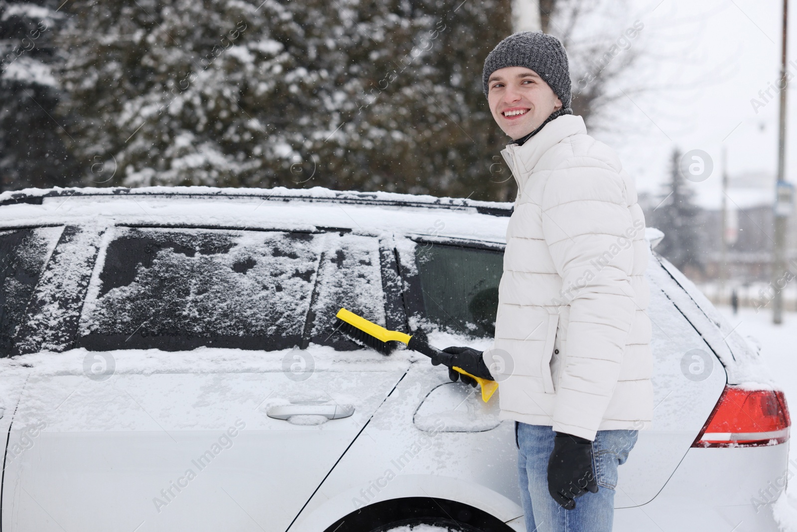 Photo of Man cleaning snow from car with brush outdoors