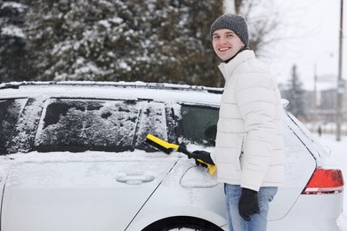 Man cleaning snow from car with brush outdoors