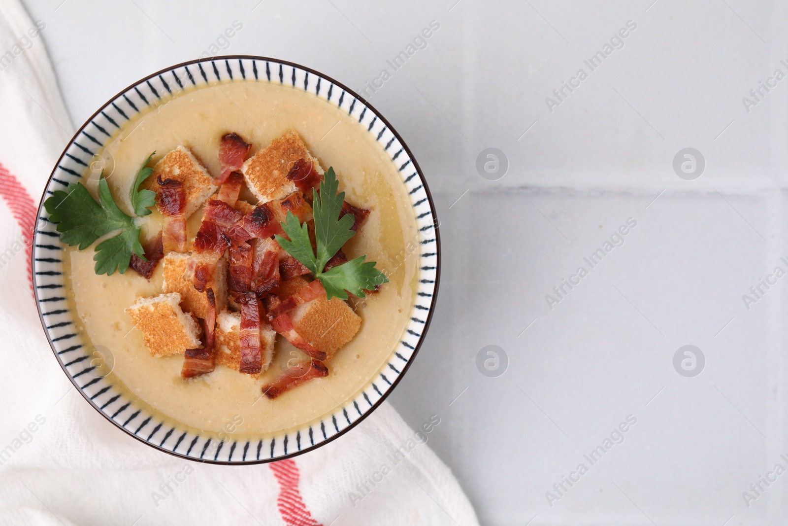 Photo of Delicious lentil soup with bacon and parsley in bowl on white tiled table, top view. Space for text