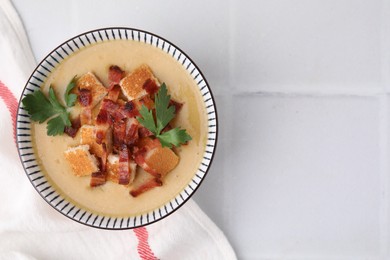 Delicious lentil soup with bacon and parsley in bowl on white tiled table, top view. Space for text