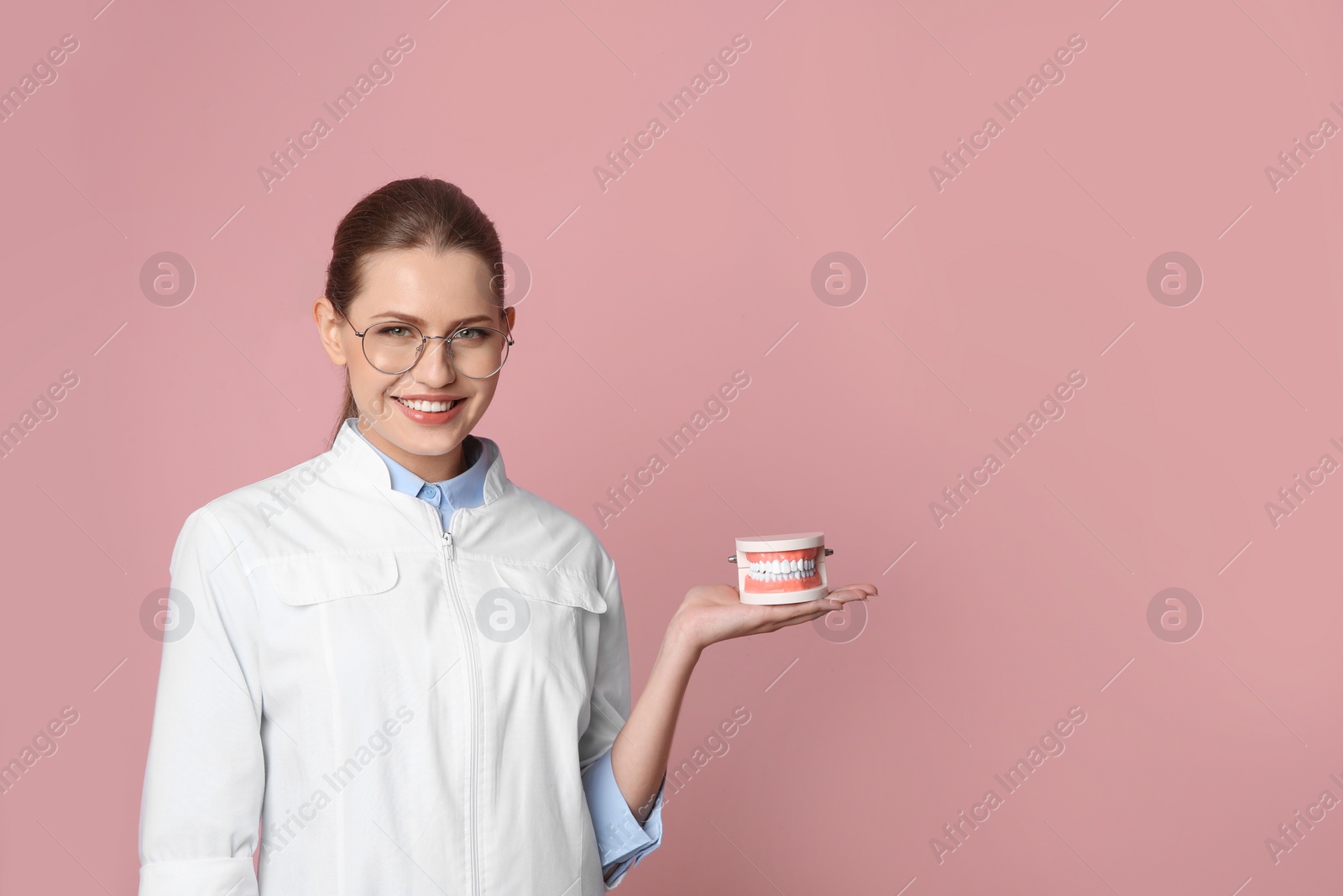 Photo of Female dentist holding jaws model on color background. Space for text