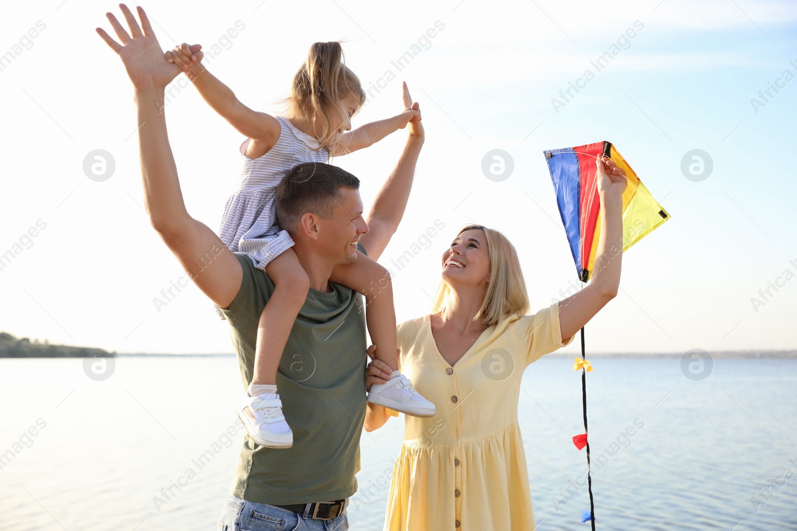 Photo of Happy parents with their child playing with kite on beach. Spending time in nature