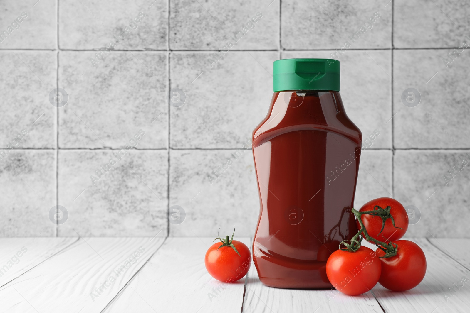 Photo of Bottle of tasty ketchup and tomatoes on white wooden table. Space for text