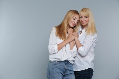 Portrait of young woman with her mature mother on grey background, space for text