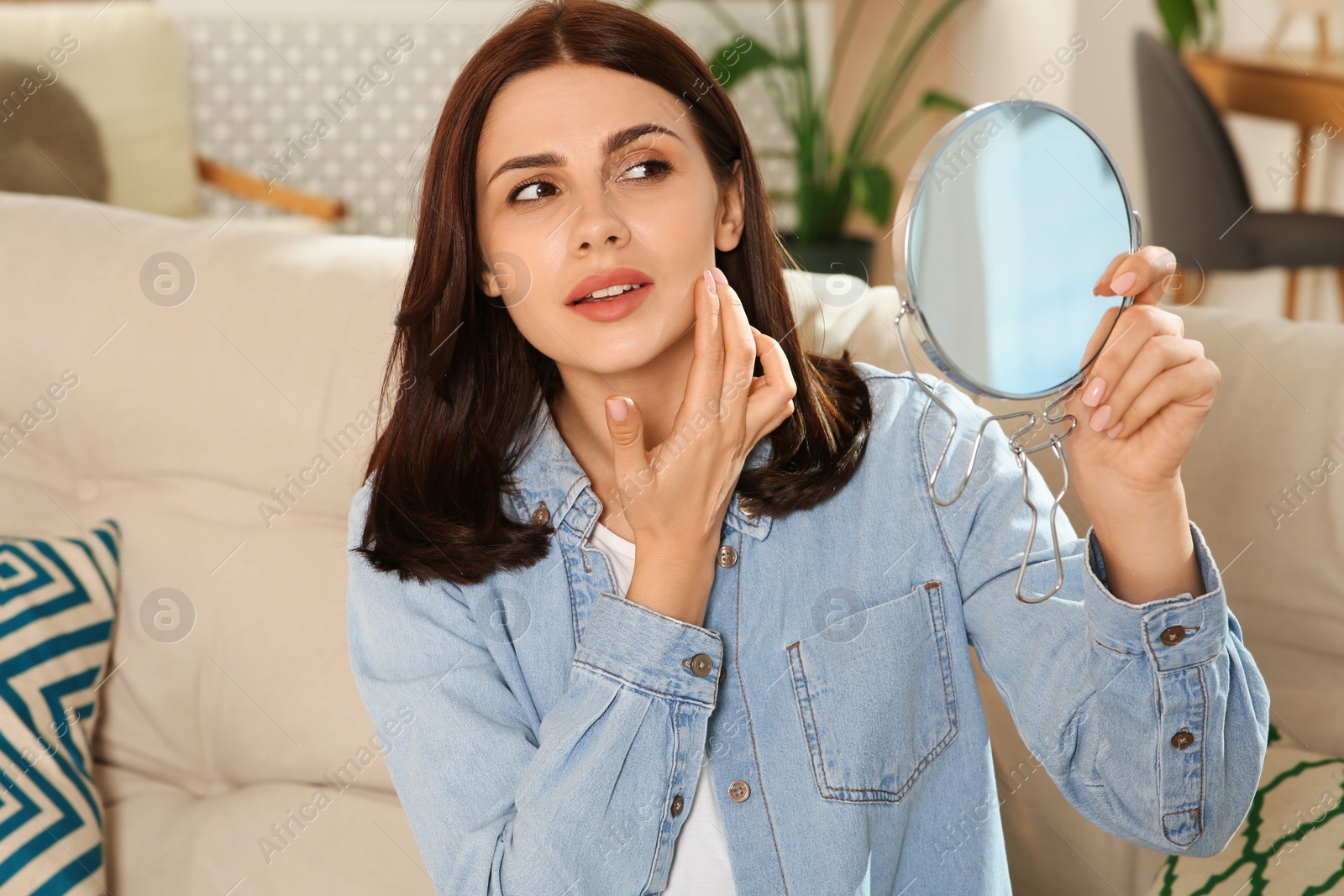 Photo of Young woman looking in mirror and squeezing pimple indoors. Hormonal disorders