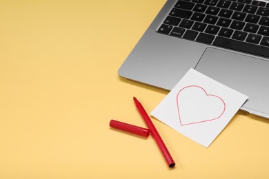 Photo of Long-distance relationship concept. Laptop, love note and red marker on pale yellow background, space for text