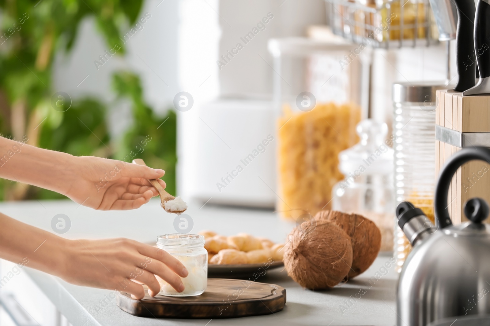 Photo of Woman taking fresh coconut oil from glass jar on table in kitchen. Healthy cooking