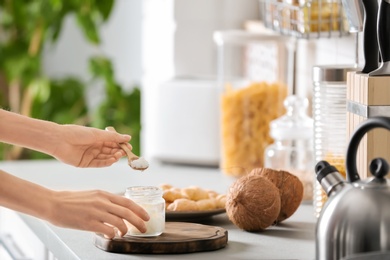 Woman taking fresh coconut oil from glass jar on table in kitchen. Healthy cooking