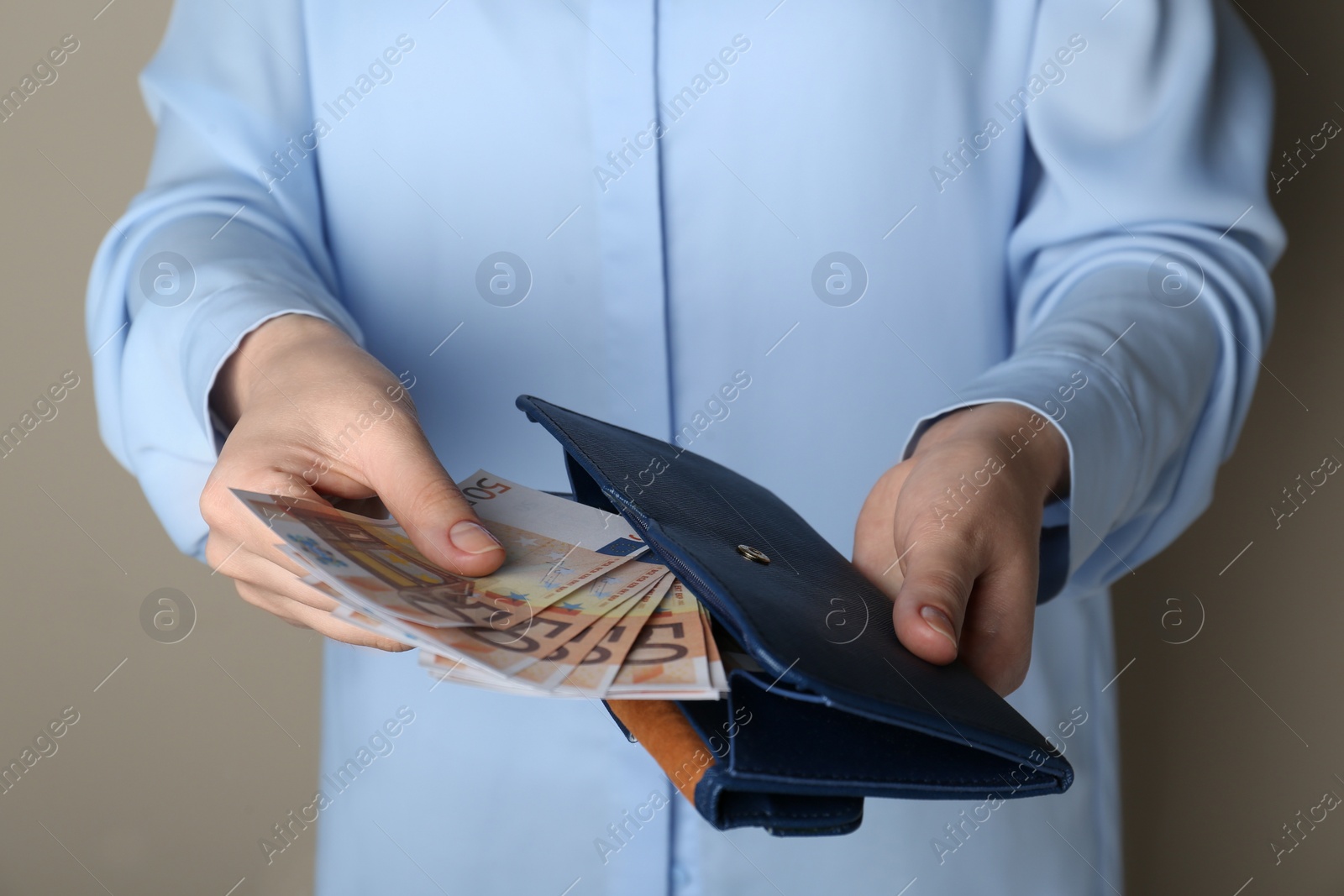 Photo of Woman holding wallet with 50 Euro banknotes on beige background, closeup. Money exchange