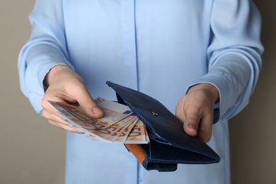 Photo of Woman holding wallet with 50 Euro banknotes on beige background, closeup. Money exchange