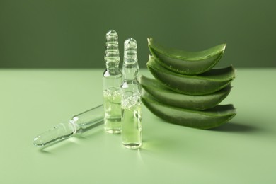 Skincare ampoules with extract of aloe vera and cut green leaves on color background