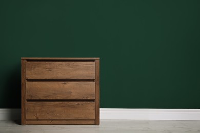 Photo of Modern wooden chest of drawers near green wall indoors. Space for text