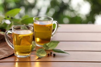 Cups of tasty iced tea with lemon on wooden table against blurred background, space for text