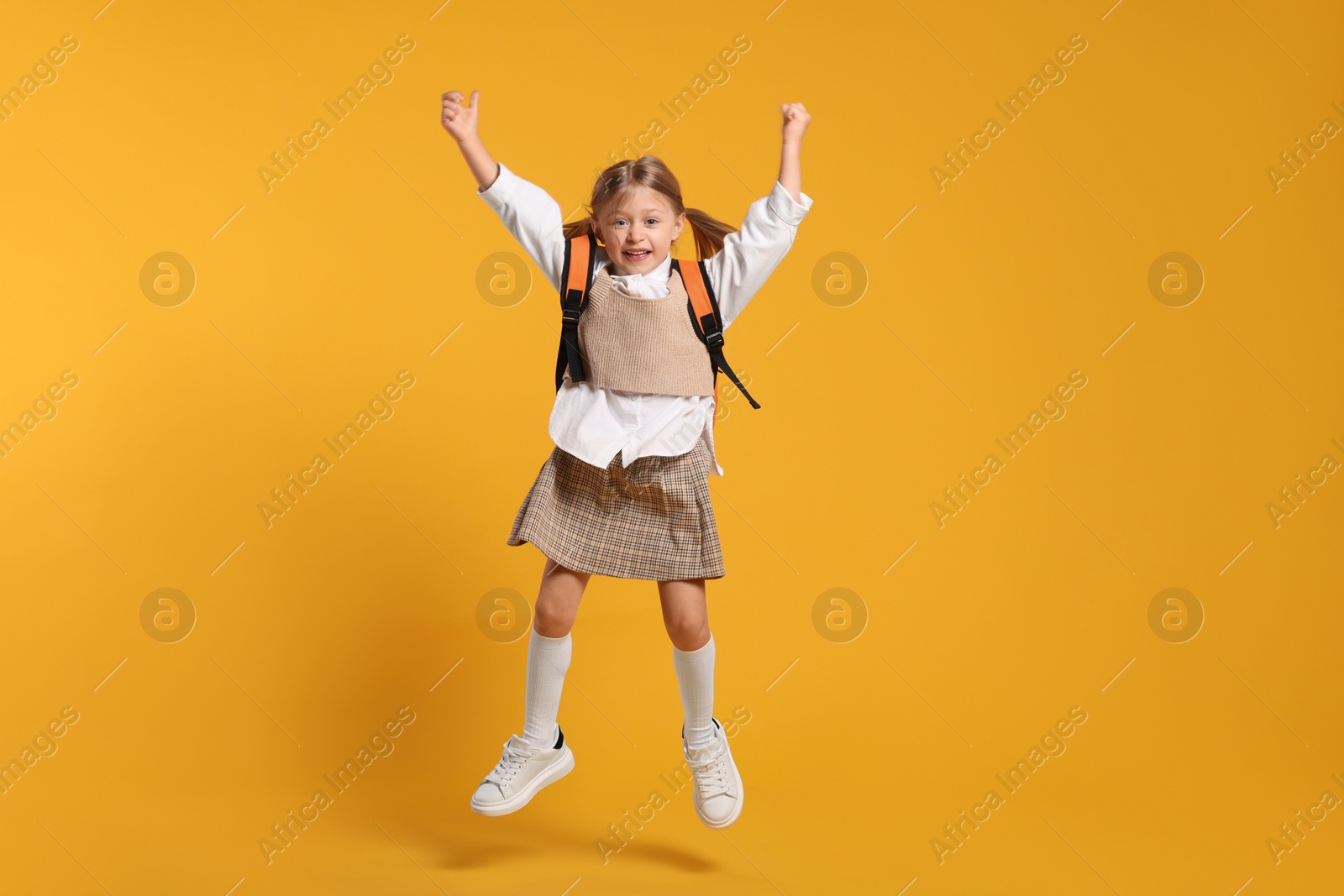 Photo of Happy schoolgirl with backpack jumping on orange background