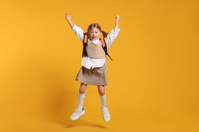 Happy schoolgirl with backpack jumping on orange background