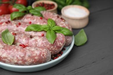 Raw homemade sausages, basil leaves and peppercorns on grey wooden table, closeup