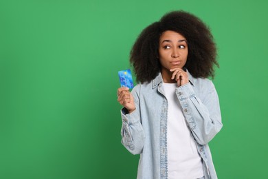 Confused woman with credit card on green background, space for text. Debt problem