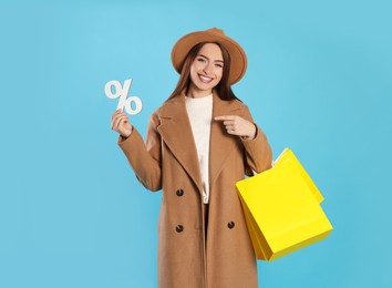 Photo of Happy young woman with shopping bags and percent symbol on light blue background. Big sale