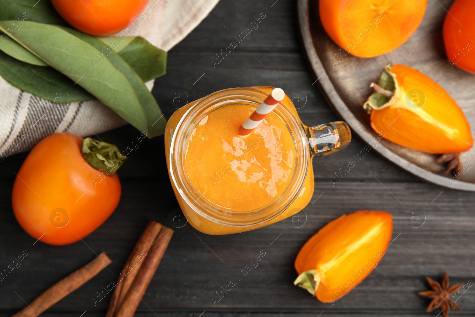 Photo of Tasty persimmon smoothie with straw on black wooden table, flat lay