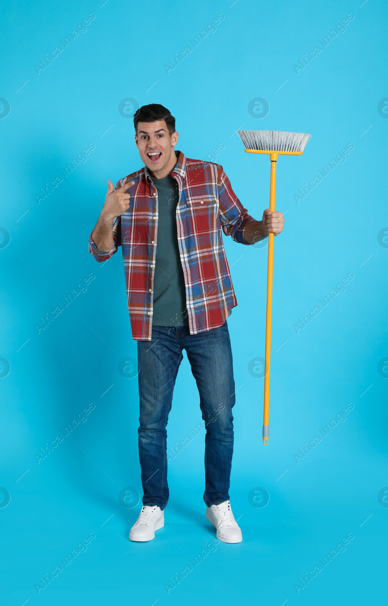 Photo of Emotional man with yellow broom on light blue background