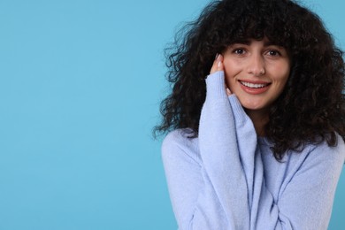 Photo of Happy young woman in stylish warm sweater on light blue background, space for text