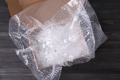 Photo of Flasks with bubble wrap and packaging foam in cardboard box on dark wooden table, top view