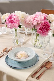 Stylish table setting with beautiful peonies and golden cutlery indoors