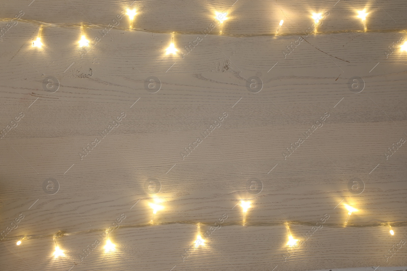 Photo of Frame of beautiful glowing Christmas lights on white wooden table, top view. Space for text