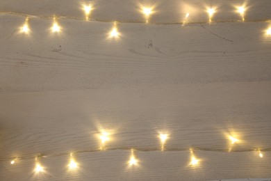 Frame of beautiful glowing Christmas lights on white wooden table, top view. Space for text