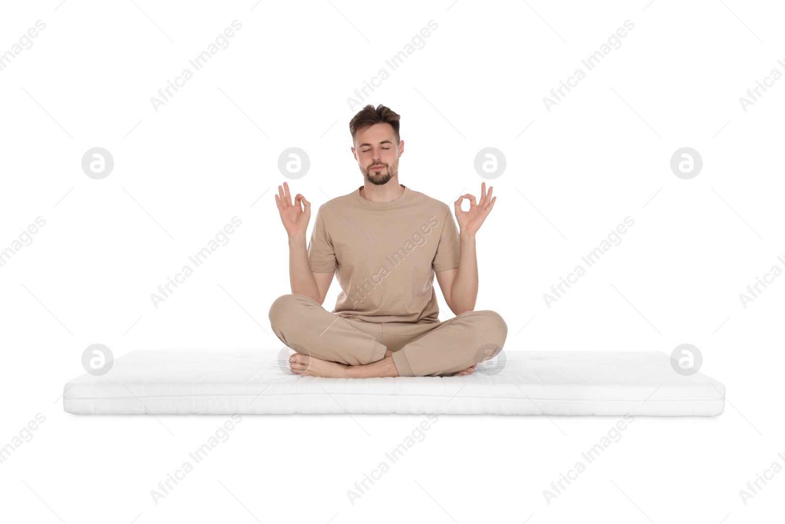 Photo of Man sitting on soft mattress and meditating against white background