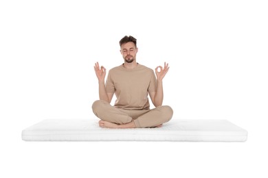 Man sitting on soft mattress and meditating against white background