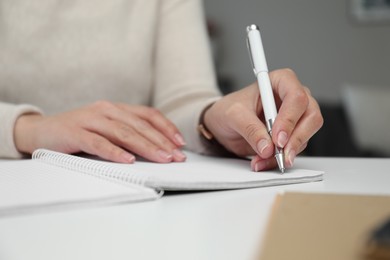 Photo of Left-handed woman writing in notebook at table indoors, closeup