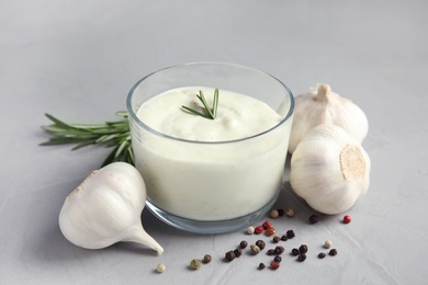 Photo of Fresh garlic bulbs, bowl of sauce, rosemary and pepper on grey background