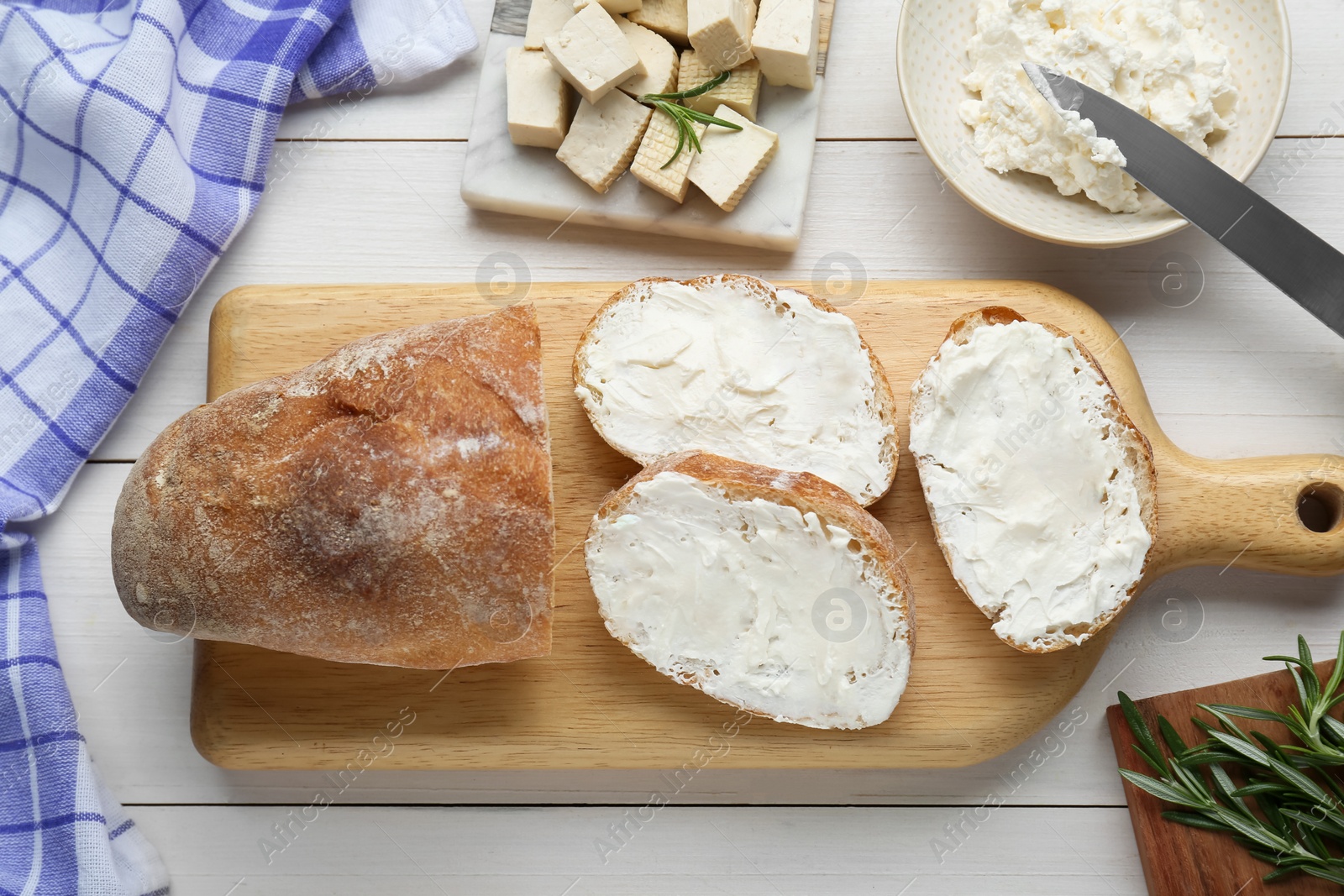 Photo of Slices of baguette with tofu cream cheese and rosemary on white wooden table, flat lay