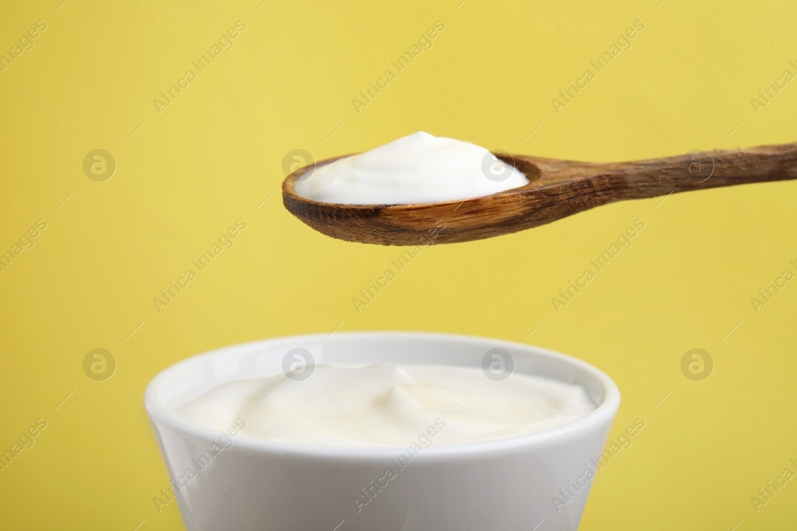 Photo of Eating delicious natural yogurt on yellow background, closeup