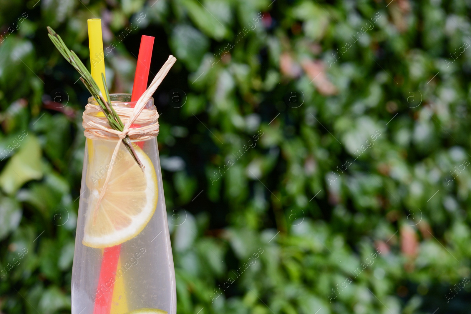 Photo of Refreshing tasty lemonade served in glass bottle against blurred background, closeup. Space for text